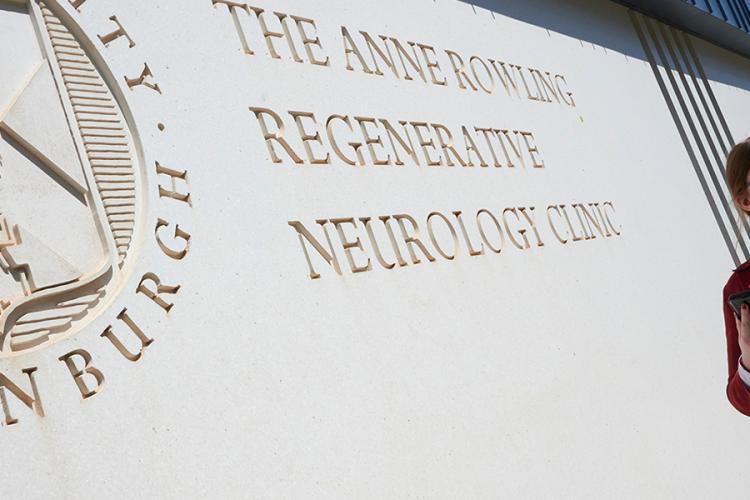 A picture taken outside the Anne Rowling Clinic building of a person walking by in a red coat with a mobile phone in their hand.