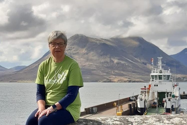 Ann Gillies sitting in front of a boat and loch