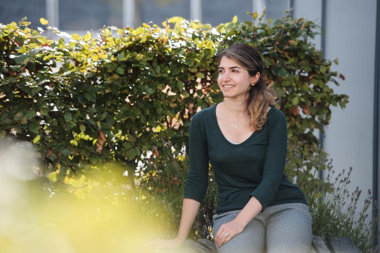 A person is pictured sitting outside, with a hedge in the background, smiling into the distance