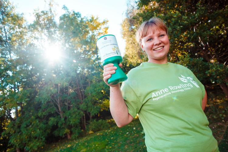 Young woman holding Anne Rowling Clinic collecting can smiling at camera