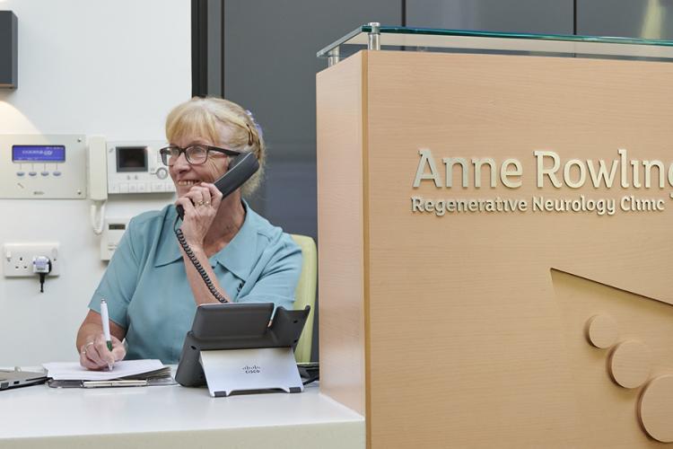 NHS Lothian receptionist sitting behind the reception desk at the Anne Rowling Clinic talking on the phone