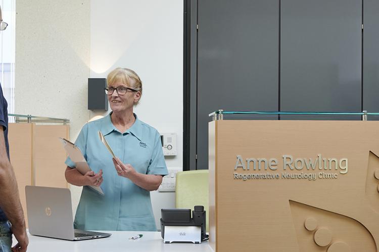 A receptionist wearing NHS uniform is greeting a patient at the Clinic front desk