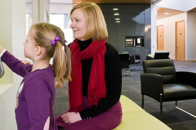 A woman watching and smiling while her young daughter plays on the "Magic Wall"; wall-mounted touchscreen device.