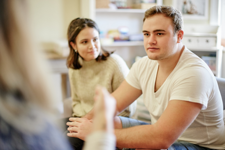 A picture of a person and their partner having a discussion with a counsellor in their home.