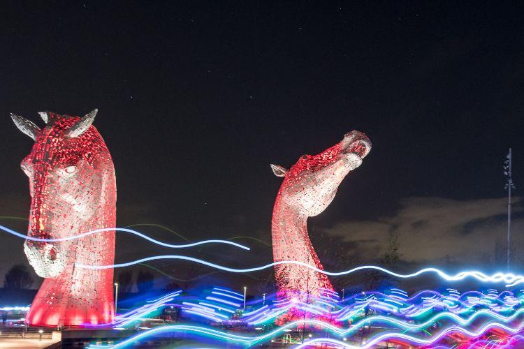The Kelpies - statues at the Helix Park in Falkirk. The statues are illuminated red against the night sky.