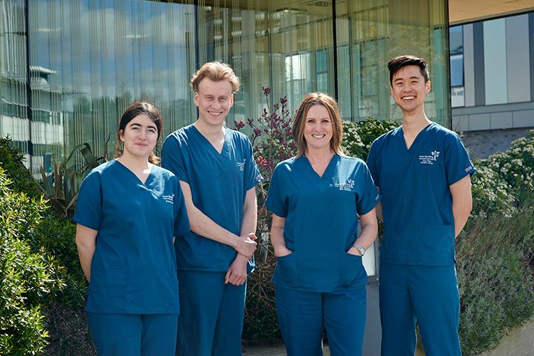 4 people wearing scrubs standing outside and smiling. Left to right: Jessica Gill, Ethan Stoker, Judith Newton, Isaac Chau.