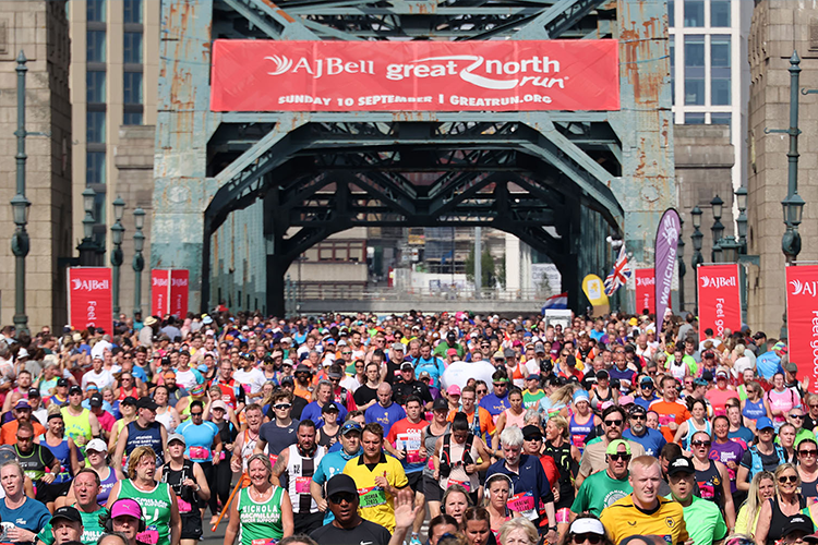 A picture taken at the start of the Great Northern Run in Tyneside. The picture has a large group of runners in different charity running tops setting off on their fundraising run