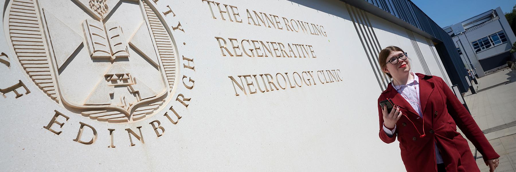 A picture taken outside the Anne Rowling Clinic building of a person walking by in a red coat with a mobile phone in their hand.