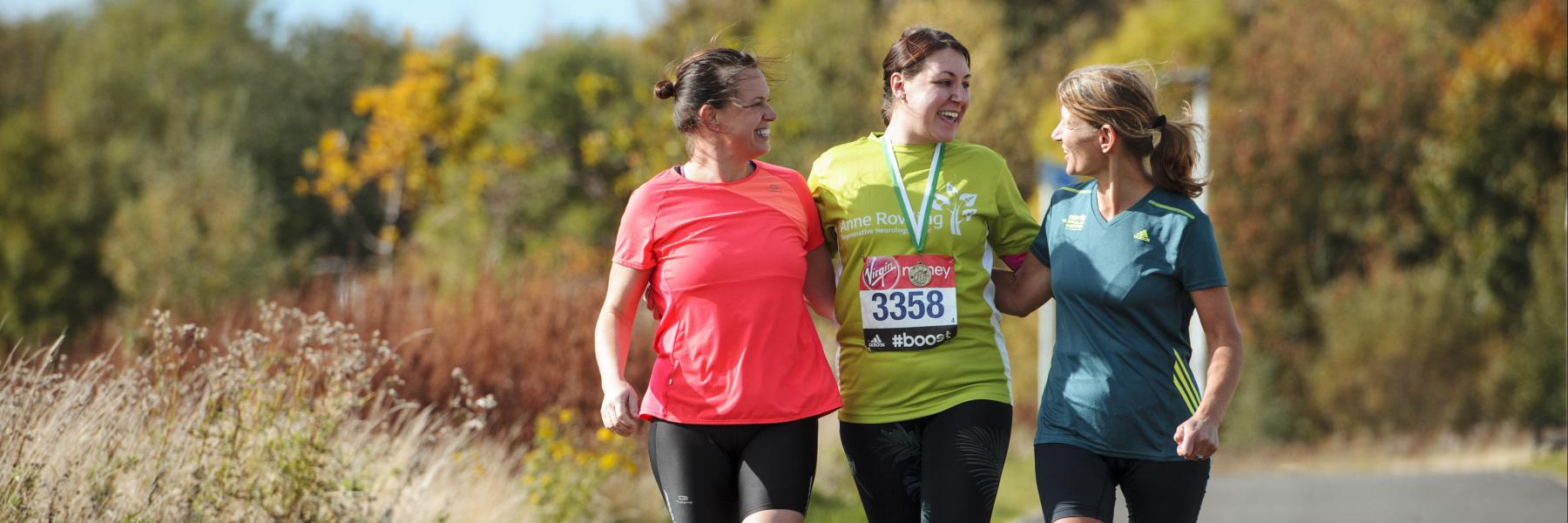 Three people pictured in running clothes, the person in the centre has an Anne Rwoling Clinic running t-shirt on and a participation medal and a running number