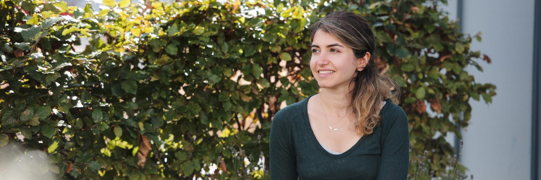 A person is pictured sitting outside, with a hedge in the background, smiling into the distance
