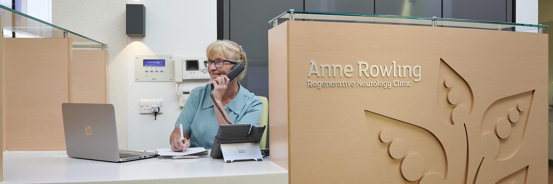 NHS Lothian receptionist sitting behind the reception desk at the Anne Rowling Clinic talking on the phone