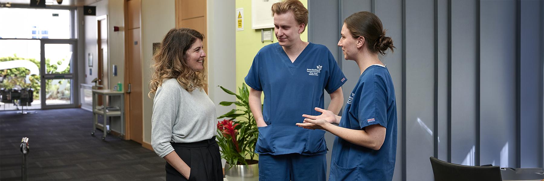 three researchers two in research scrub uniform talking in the reception area of the Anne Rowling Clinic building