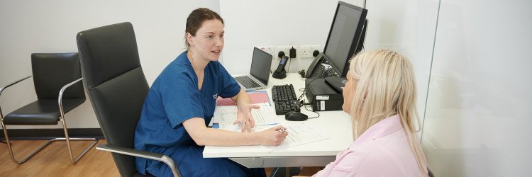 A research nurse and a patient are in discussion in a clinic room, the nurse is making notes