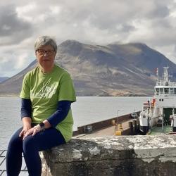 Ann Gillies sitting in front of a boat and loch