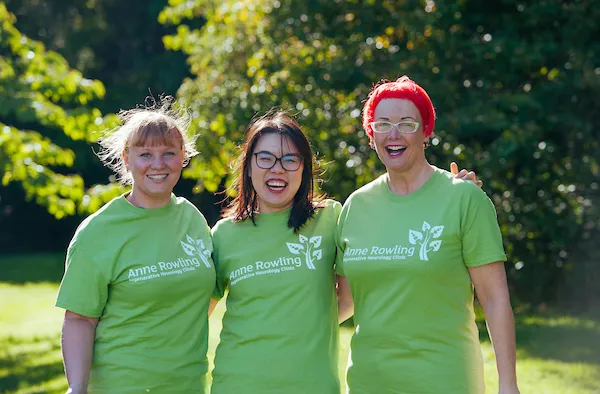 3 people dressed in green Anne Rowling Clinic T-shirts linking arms and smiling